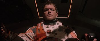 Movie still from “The Martian” (2015), directed by Ridley Scott – A man in a space suit is posing for a picture; Close Up shot, Low angle