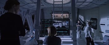 Movie still from “The Martian” (2015), directed by Ridley Scott – A woman sitting in front of a large screen television; Wide shot, Over the shoulder angle