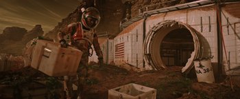Movie still from “The Martian” (2015), directed by Ridley Scott – A man in a spacesuit is standing next to a crate; Wide shot, Low angle