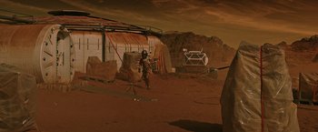Movie still from “The Martian” (2015), directed by Ridley Scott – A man in a helmet and a suit is standing on a dirt field; Extreme Wide shot, High angle