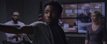 Movie still from “The Martian” (2015), directed by Ridley Scott – A person in a room with a flag in the background; Close Up shot, Over the shoulder angle