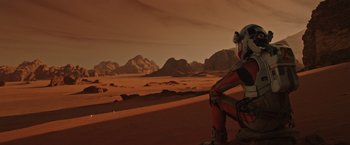 Movie still from “The Martian” (2015), directed by Ridley Scott – An astronaut sitting on the side of a desert road; Wide shot, High angle