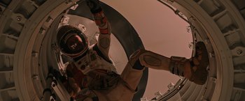 Movie still from “The Martian” (2015), directed by Ridley Scott – A man in a space suit hanging from a metal ring; Wide shot, Overhead angle