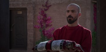 Movie still from “The Matchmaker” (2023), directed by Abdulmohsen Aldhabaan – A man with a beard holding a pillow in front of a wall; Medium shot, Over the shoulder angle
