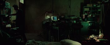 Movie still from “The Matrix” (1999), directed by Lana Wachowski – Two computers on a desk in a dark room; Wide shot, High angle