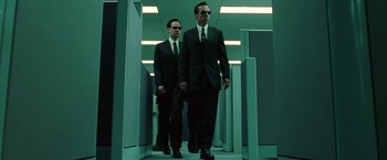 Movie still from “The Matrix” (1999), directed by Lana Wachowski – A couple of men in suits walking down a hall way; Wide shot, Low angle