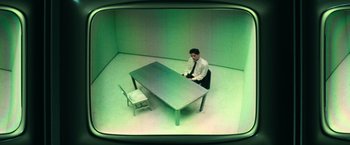 Movie still from “The Matrix” (1999), directed by Lana Wachowski – A man sitting at a table in an empty room; Wide shot, High angle