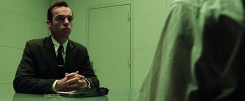 Movie still from “The Matrix” (1999), directed by Lana Wachowski – A man sitting at a table in front of another man; Medium shot, Over the shoulder angle