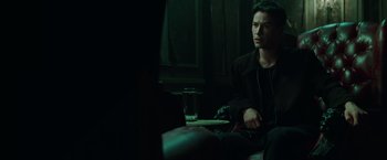 Movie still from “The Matrix” (1999), directed by Lana Wachowski – A man sitting on a couch in a dark room; Medium shot, Over the shoulder angle