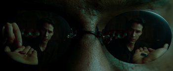 Movie still from “The Matrix” (1999), directed by Lana Wachowski – A man with a pair of glasses on his face; Extreme Close Up shot, Over the shoulder angle