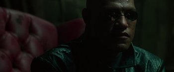 Movie still from “The Matrix” (1999), directed by Lana Wachowski – A person wearing glasses in a dark room; Close Up shot, High angle