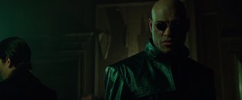 Movie still from “The Matrix” (1999), directed by Lana Wachowski – A man in a leather jacket wearing a pair of sunglasses; Close Up shot, Low angle