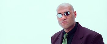 Movie still from “The Matrix” (1999), directed by Lana Wachowski – A bald man wearing a suit and sunglasses; Close Up shot, Low angle