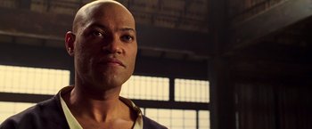 Movie still from “The Matrix” (1999), directed by Lana Wachowski – A man with a bald head looking into the distance; Close Up shot, Low angle