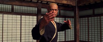 Movie still from “The Matrix” (1999), directed by Lana Wachowski – A man in a black and yellow outfit is practicing martial arts in front of a wall; Medium shot, Low angle