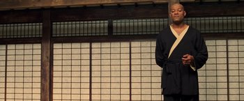 Movie still from “The Matrix” (1999), directed by Lana Wachowski – A man standing in front of an asian style wall; Medium shot, Low angle