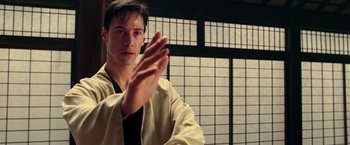 Movie still from “The Matrix” (1999), directed by Lana Wachowski – A man in a white robe is practicing martial arts in front of a window; Close Up shot, Over the shoulder angle