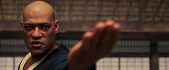 Movie still from “The Matrix” (1999), directed by Lana Wachowski – A bald headed man with his hands raised; Close Up shot, Over the shoulder angle