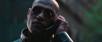 Movie still from “The Matrix” (1999), directed by Lana Wachowski – A bald man wearing sunglasses talking on a cell phone; Close Up shot, Low angle