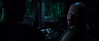 Movie still from “The Matrix” (1999), directed by Lana Wachowski – A man in front of computer screens with green lights; Close Up shot, Over the shoulder angle
