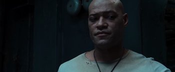 Movie still from “The Matrix” (1999), directed by Lana Wachowski – A bald man with a necklace is looking at the camera; Close Up shot, Low angle