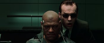 Movie still from “The Matrix” (1999), directed by Lana Wachowski – A man with headphones and a man with sunglasses; Close Up shot, Over the shoulder angle