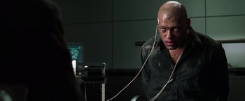 Movie still from “The Matrix” (1999), directed by Lana Wachowski – A bald man wearing headphones and sitting in front of a computer; Close Up shot, High angle