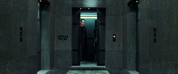 Movie still from “The Matrix” (1999), directed by Lana Wachowski – A man standing in an elevator looking out of the door; Wide shot, Low angle