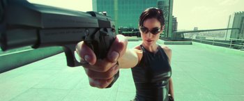 Movie still from “The Matrix” (1999), directed by Lana Wachowski – A woman holding a gun pointed at the camera; Medium shot, Low angle