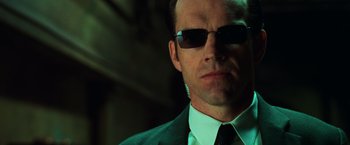 Movie still from “The Matrix” (1999), directed by Lana Wachowski – A person wearing a suit and sunglasses; Close Up shot, Low angle