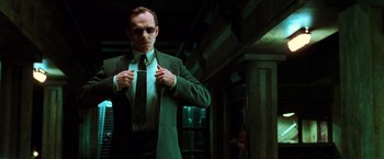 Movie still from “The Matrix” (1999), directed by Lana Wachowski – A man in a suit and sunglasses putting on a tie; Medium shot, Low angle