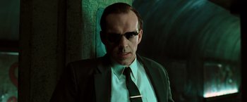Movie still from “The Matrix” (1999), directed by Lana Wachowski – A person wearing a suit and sunglasses; Close Up shot, Low angle