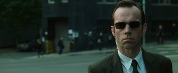 Movie still from “The Matrix” (1999), directed by Lana Wachowski – A person wearing a suit and sunglasses; Close Up shot, Over the shoulder angle