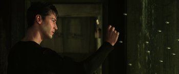 Movie still from “The Matrix” (1999), directed by Lana Wachowski – A man standing in a dark room holding something up; Close Up shot, Low angle