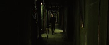 Movie still from “The Matrix” (1999), directed by Lana Wachowski – A man walking down a hallway in a dark room; Wide shot, High angle