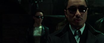 Movie still from “The Matrix Reloaded” (2003), directed by Lana Wachowski – A man and a woman wearing sunglasses in a dark room; Close Up shot, Low angle