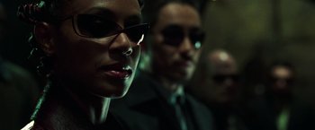 Movie still from “The Matrix Reloaded” (2003), directed by Lana Wachowski – A man and a woman wearing sunglasses and a suit; Close Up shot, Low angle
