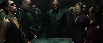 Movie still from “The Matrix Reloaded” (2003), directed by Lana Wachowski – A group of men standing next to each other in front of a table; Medium shot, High angle