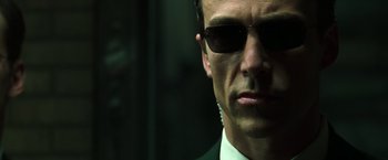 Movie still from “The Matrix Reloaded” (2003), directed by Lana Wachowski – A person wearing a suit and sunglasses; Close Up shot, Low angle