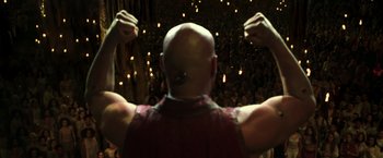 Movie still from “The Matrix Reloaded” (2003), directed by Lana Wachowski – A bald man with his hands up in front of a crowd; Medium shot, Low angle