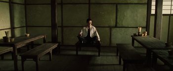 Movie still from “The Matrix Reloaded” (2003), directed by Lana Wachowski – A man sitting on top of a wooden bench in a room; Wide shot, High angle