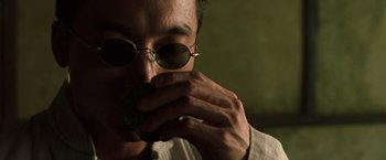 Movie still from “The Matrix Reloaded” (2003), directed by Lana Wachowski – A man with glasses is holding something to his face; Close Up shot, Over the shoulder angle