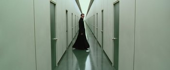 Movie still from “The Matrix Reloaded” (2003), directed by Lana Wachowski – A man in a long black coat walking down a hallway; Wide shot, High angle