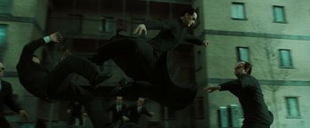 Movie still from “The Matrix Reloaded” (2003), directed by Lana Wachowski – A man is jumping in the air while another man watches; Wide shot, Low angle