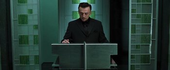 Movie still from “The Matrix Reloaded” (2003), directed by Lana Wachowski – A man in a black suit writing on a piece of paper; Medium shot, Low angle