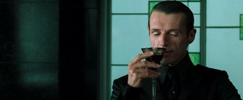Movie still from “The Matrix Reloaded” (2003), directed by Lana Wachowski – A man in a black suit drinking a glass of wine; Close Up shot, Low angle