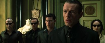 Movie still from “The Matrix Reloaded” (2003), directed by Lana Wachowski – A group of men standing next to each other in suits; Close Up shot, Over the shoulder angle