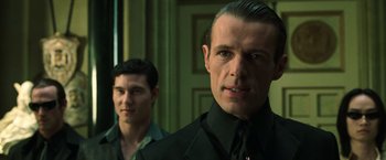 Movie still from “The Matrix Reloaded” (2003), directed by Lana Wachowski – A man in a suit and tie standing next to another man in a suit and tie; Close Up shot, Over the shoulder angle