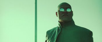 Movie still from “The Matrix Reloaded” (2003), directed by Lana Wachowski – A bald man wearing sunglasses and a green outfit; Close Up shot, Low angle