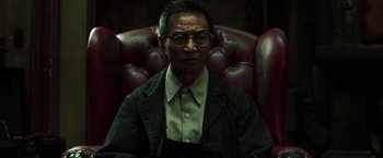 Movie still from “The Matrix Reloaded” (2003), directed by Lana Wachowski – An older man sitting in a chair wearing a jacket; Medium shot, Low angle